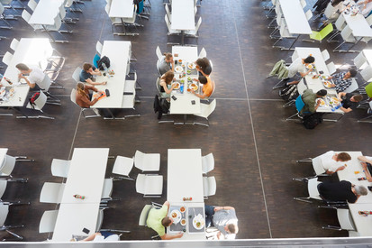 Auf dem Bild sieht man den Blick von oben in die Mensa der Hochschule Kaiserslautern. Studierende sitzen an Tischen und essen.